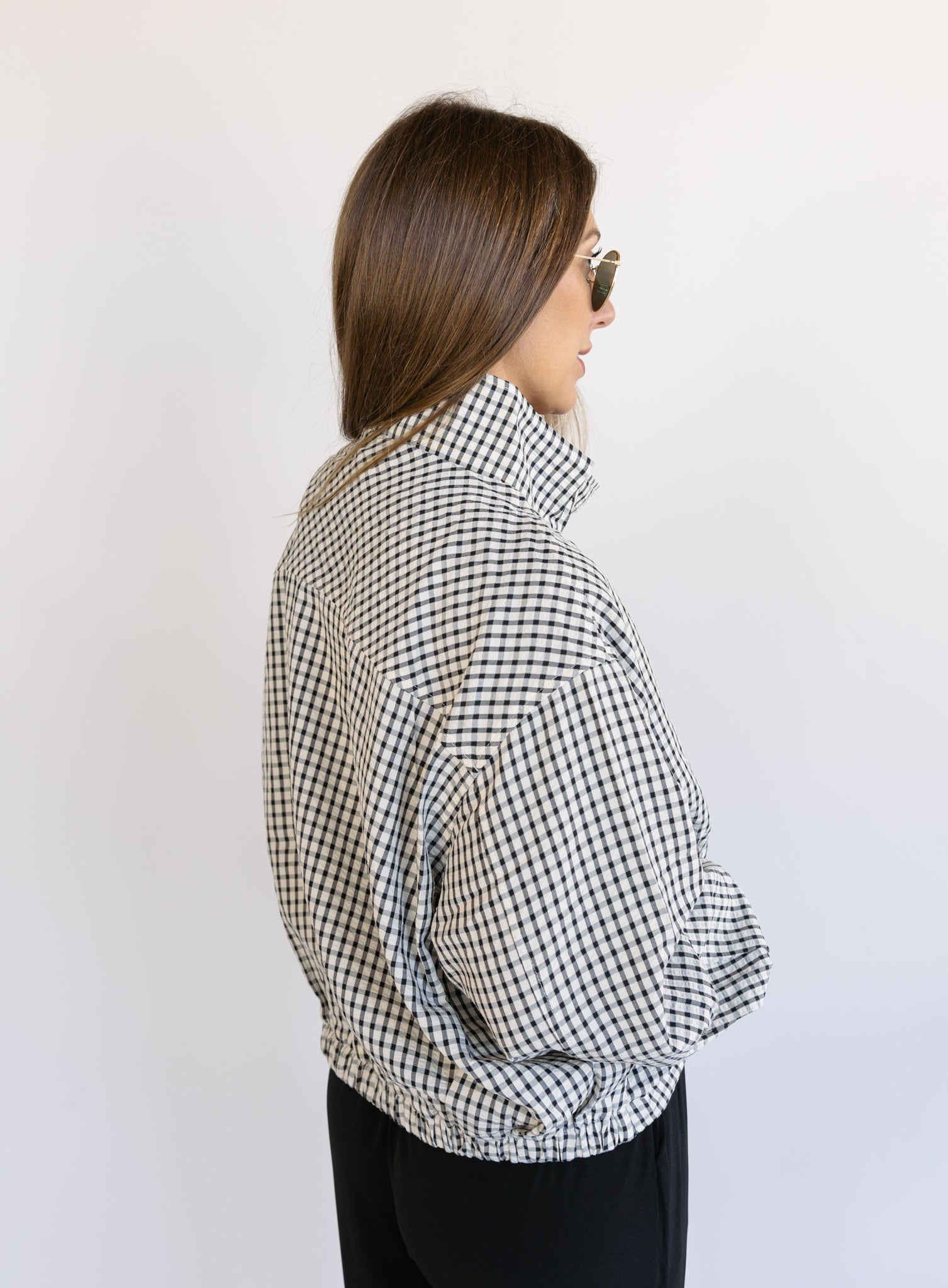 Woman wearing the Calliope Funnel Neck Bomber Jacket, a black and white gingham zip-up bomber