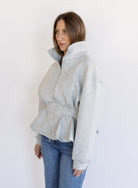 Woman wearing the Annika Peplum Zip Jacket, a heather grey knit zip-up with a funnel collar and peplum hem