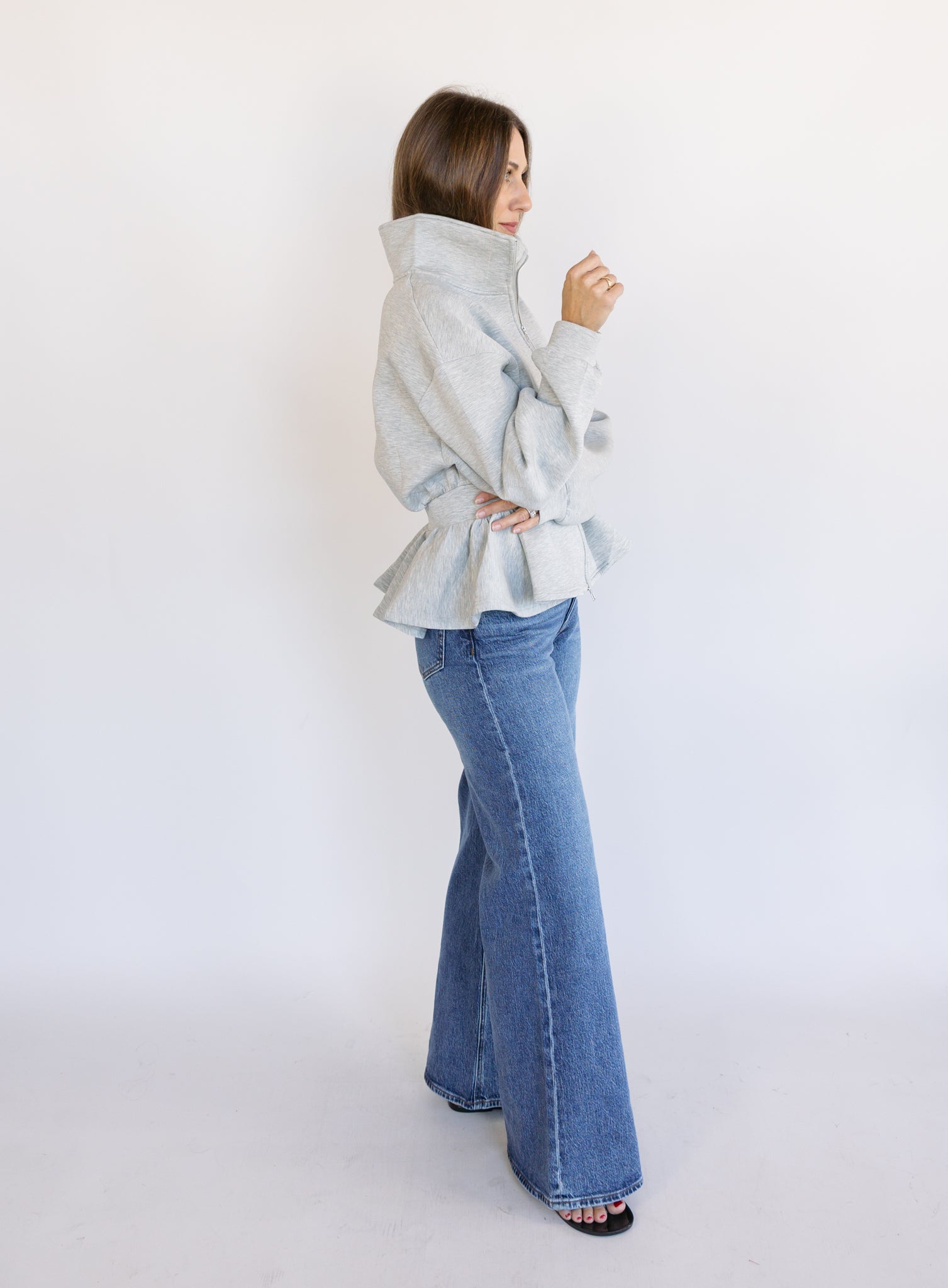 Woman wearing the Annika Peplum Zip Jacket, a heather grey knit zip-up with a funnel collar and peplum hem