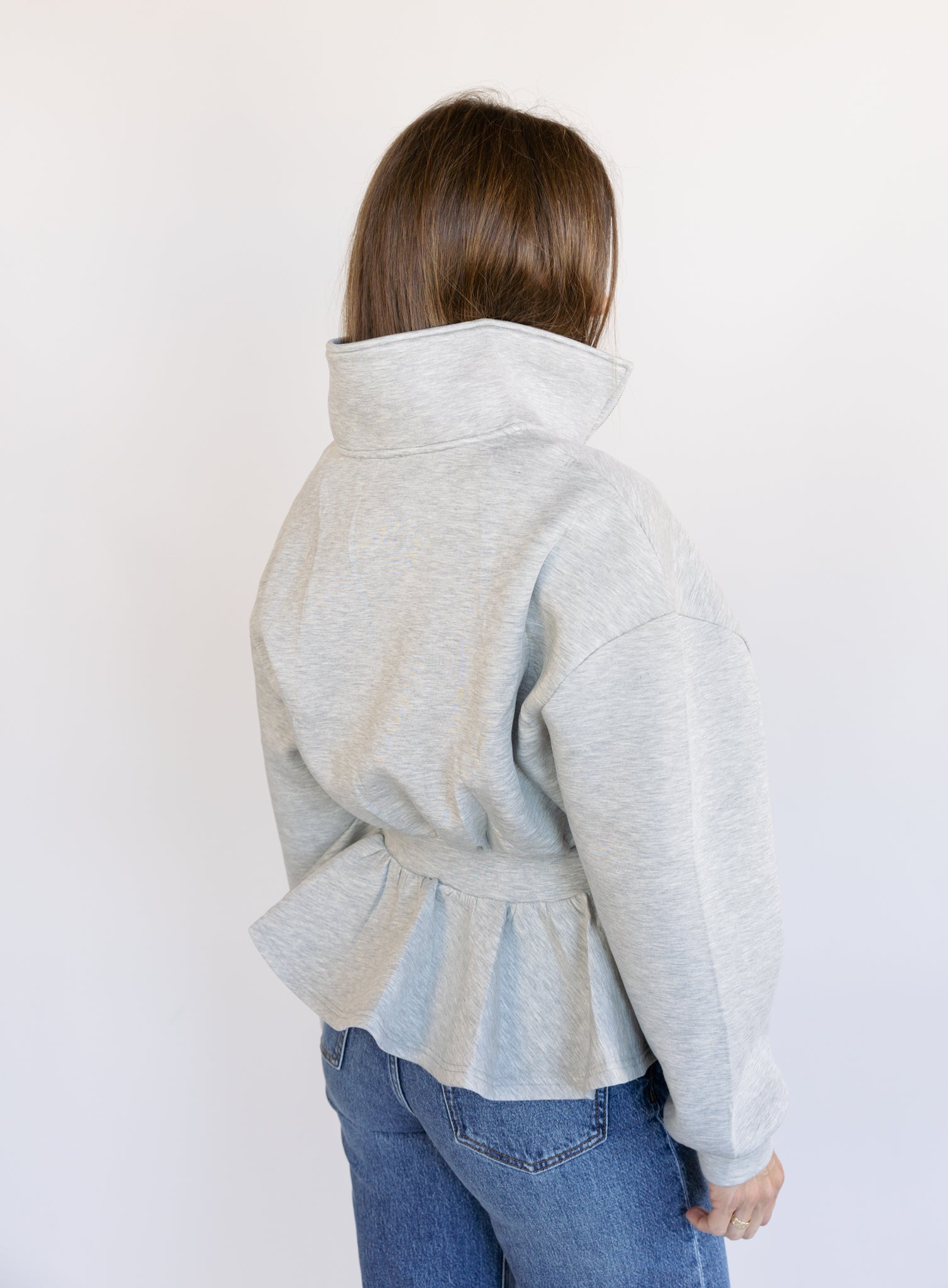 Woman wearing the Annika Peplum Zip Jacket, a heather grey knit zip-up with a funnel collar and peplum hem