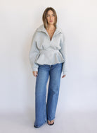 Woman wearing the Annika Peplum Zip Jacket, a heather grey knit zip-up with a funnel collar and peplum hem