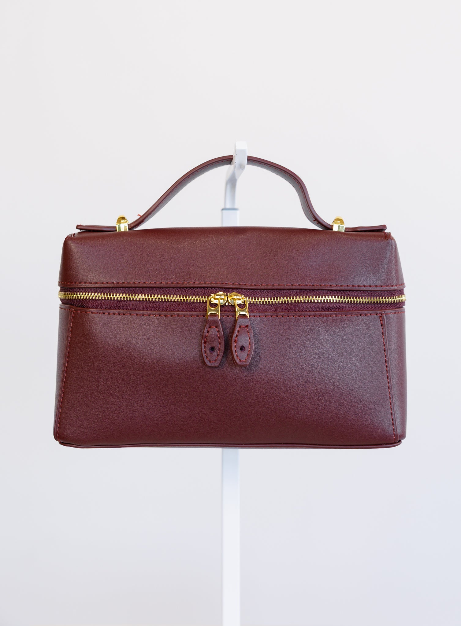 Sabine Bag, a burgundy boxy top-handle bag with gold hardware and a crossbody strap