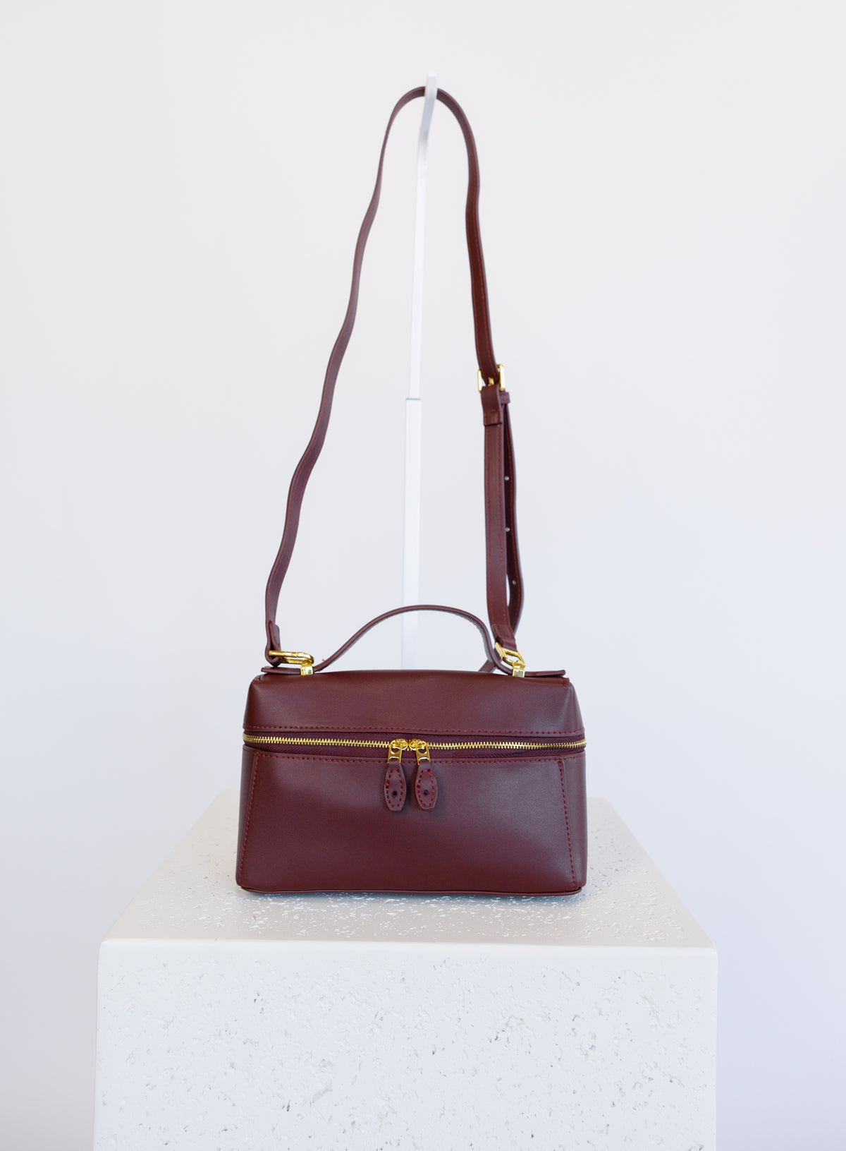 Sabine Bag, a burgundy boxy top-handle bag with gold hardware and a crossbody strap
