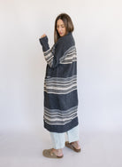 Woman wearing the Linnea Striped Sweater Coat, a long charcoal knit coat with cream and taupe stripes