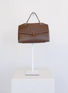Beatrice Satchel, a brown ostrich-embossed top-handle bag with a gold bar clasp