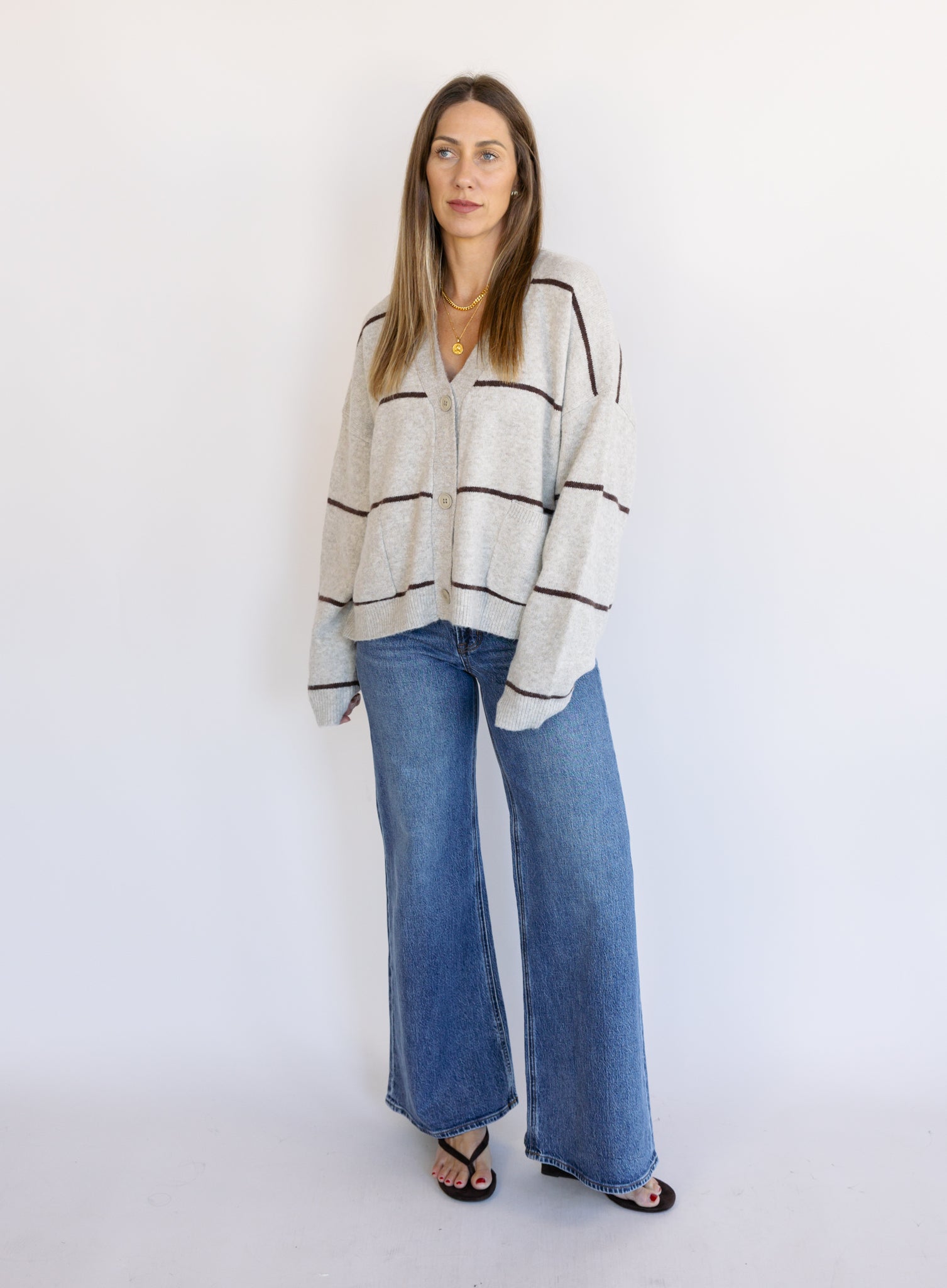 Woman wearing the Juno Striped Knit Cardigan, a mushroom knit cardigan with chocolate stripes and a V-neck