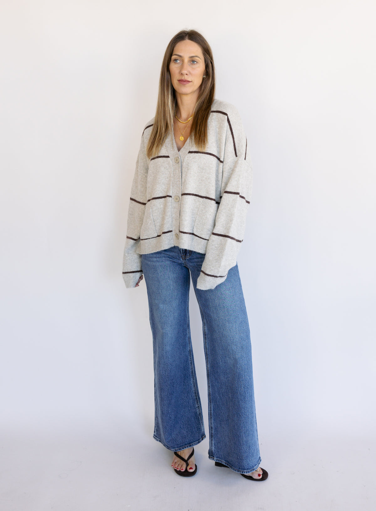 Woman wearing the Juno Striped Knit Cardigan, a mushroom knit cardigan with chocolate stripes and a V-neck