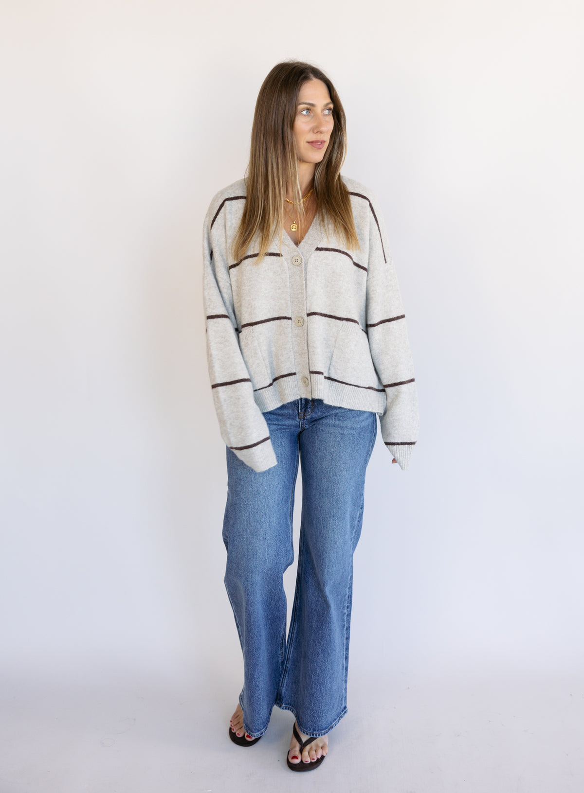 Woman wearing the Juno Striped Knit Cardigan, a mushroom knit cardigan with chocolate stripes and a V-neck
