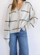 Woman wearing the Juno Striped Knit Cardigan, a mushroom knit cardigan with chocolate stripes and a V-neck