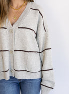 Woman wearing the Juno Striped Knit Cardigan, a mushroom knit cardigan with chocolate stripes and a V-neck