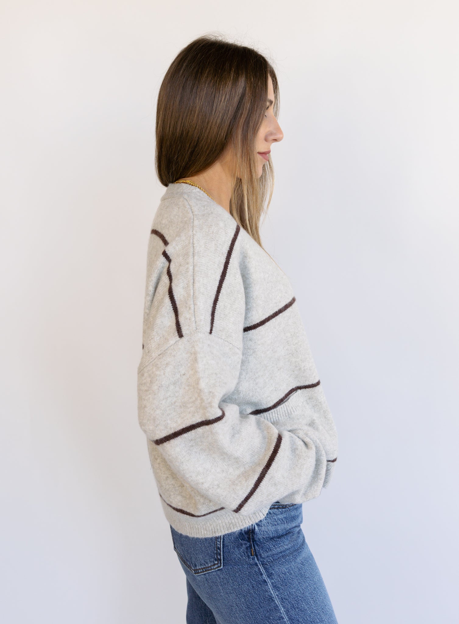 Woman wearing the Juno Striped Knit Cardigan, a mushroom knit cardigan with chocolate stripes and a V-neck