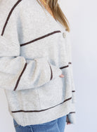 Woman wearing the Juno Striped Knit Cardigan, a mushroom knit cardigan with chocolate stripes and a V-neck